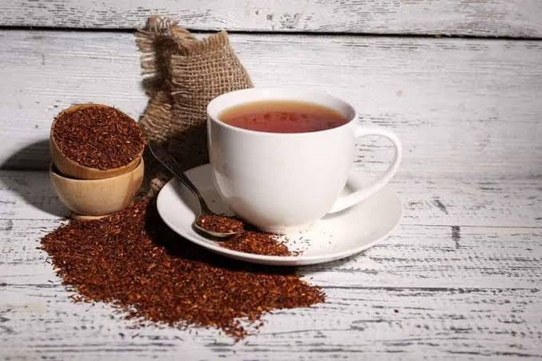  Tách trà rooibos màu đỏ nâu cùng lá khô bên cạnh